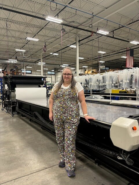 Cara posing in front of a fabric cutting machine